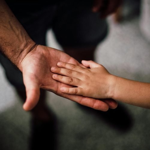Close-up of a child's hand resting gently on a man's hand, symbolizing love and support.